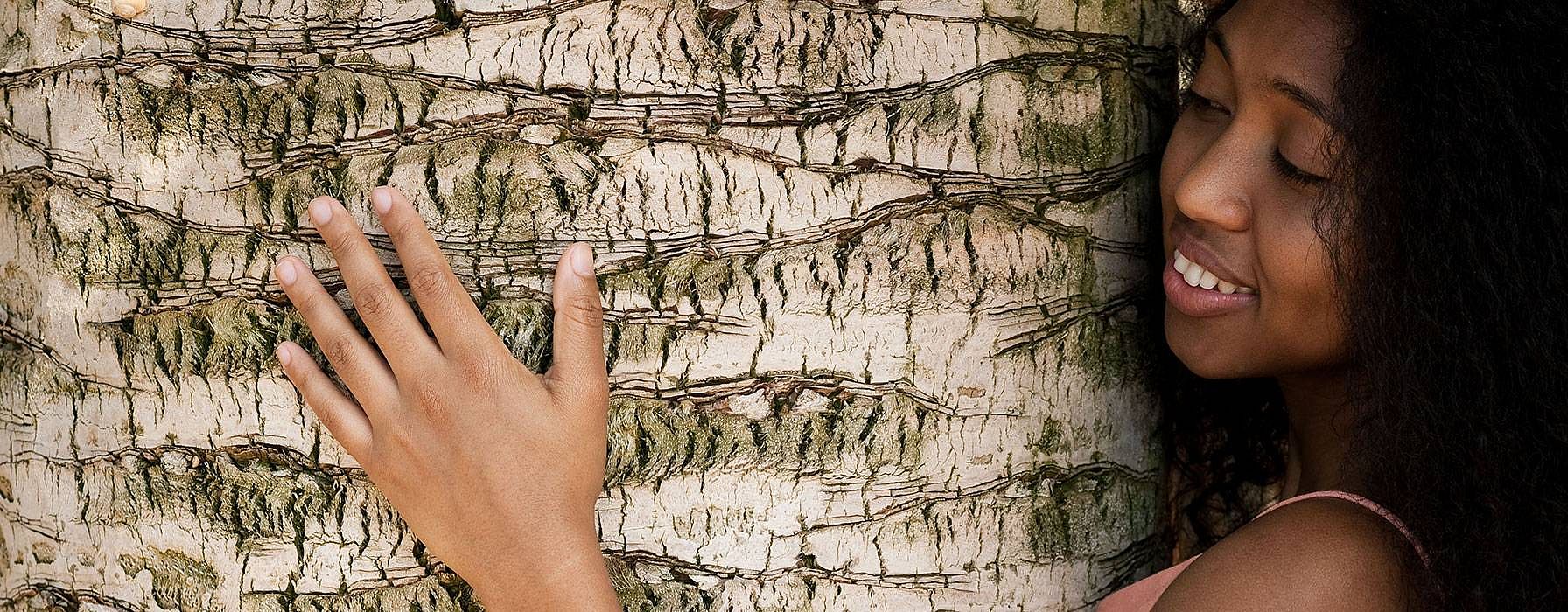 dark skinned woman hugging a tree.