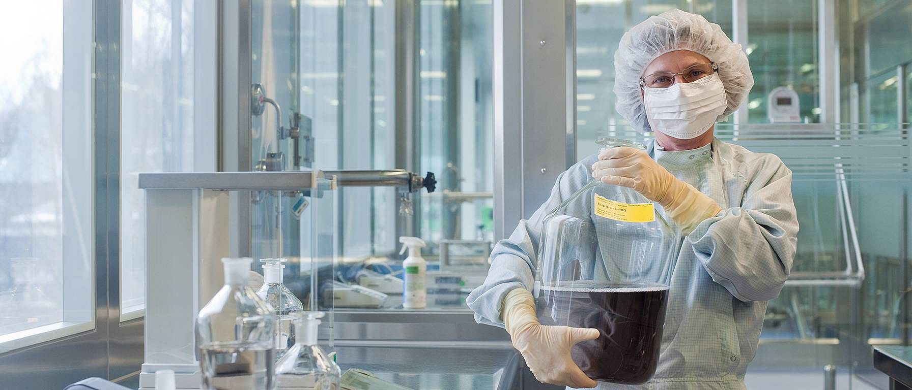 Lab assistant holding a large transparent container filled with a dark liquid