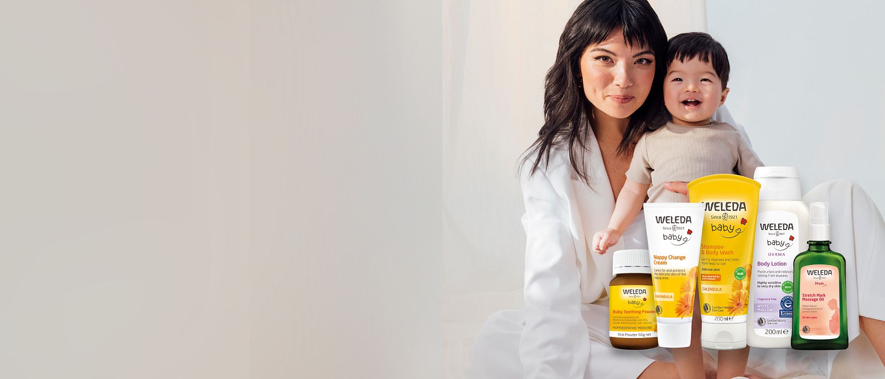 Mother holding baby with Weleda products infront.
