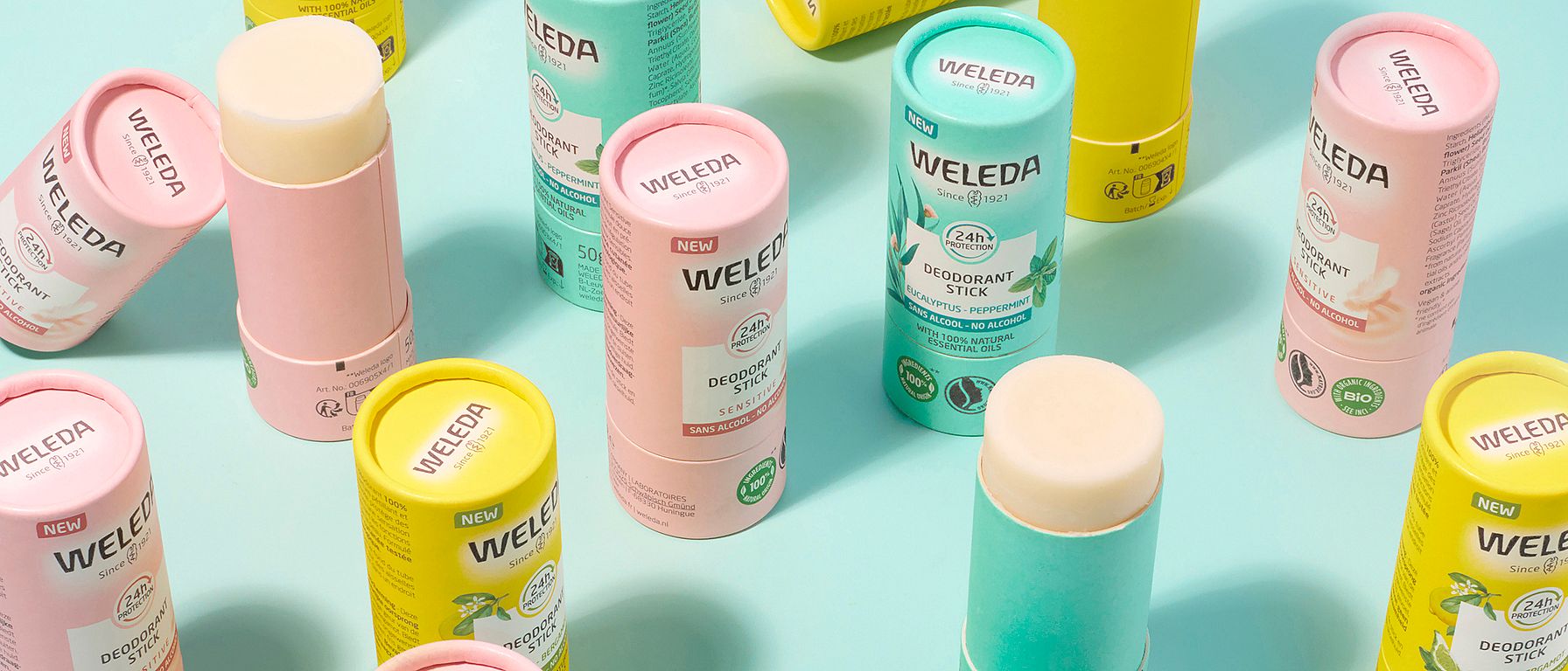 Weleda Deodorant Sticks group shot with open tops against turquoise background.