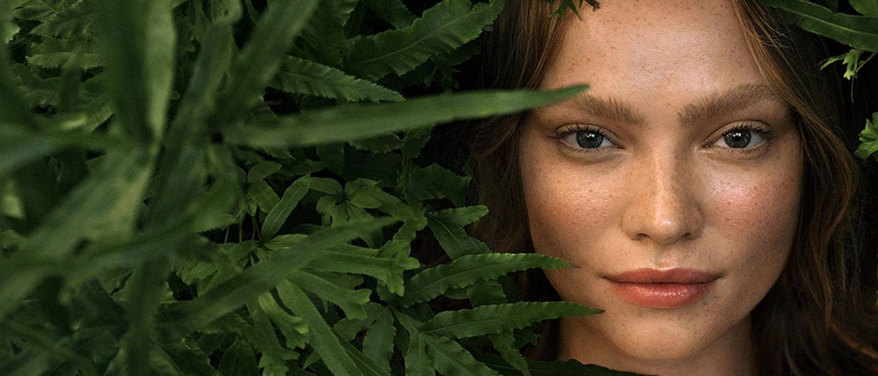 Woman's face next to green leafs.