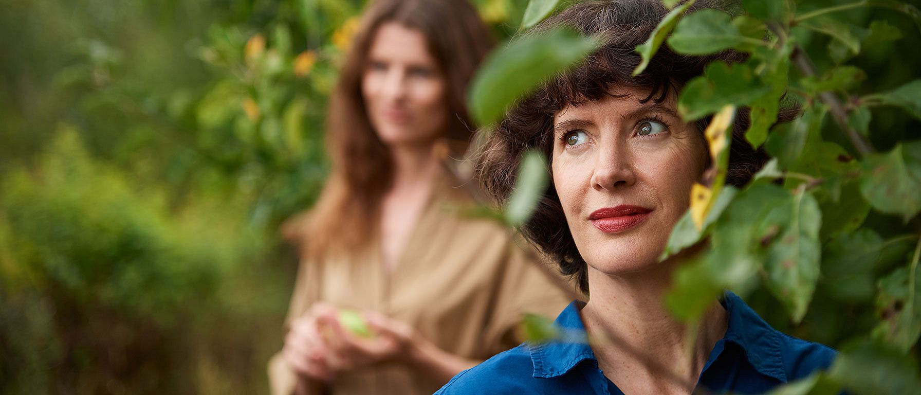 Women standing behind tree leaves.