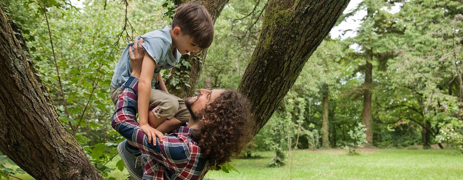 Man holding a child above his arms in a forest.
