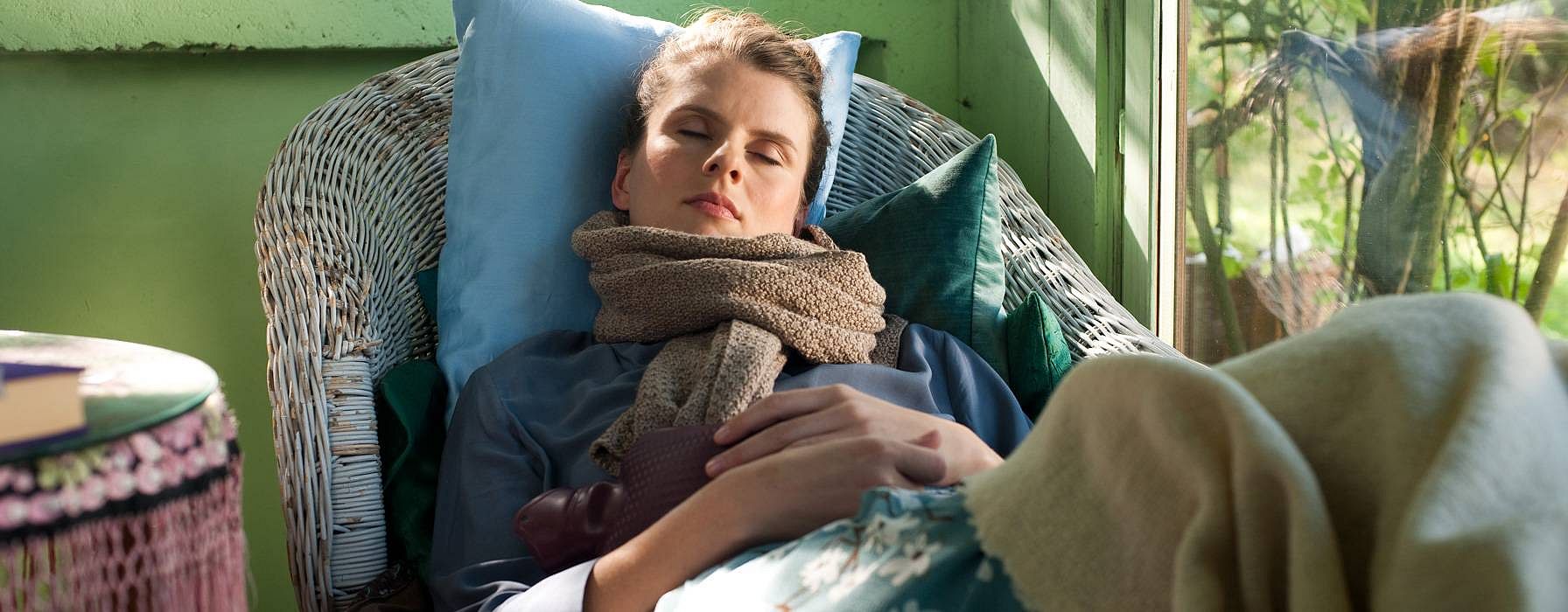 Woman sleeping on a cane chair wearing a scarf.