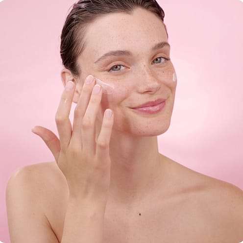 Young woman applies white cream to her skin.