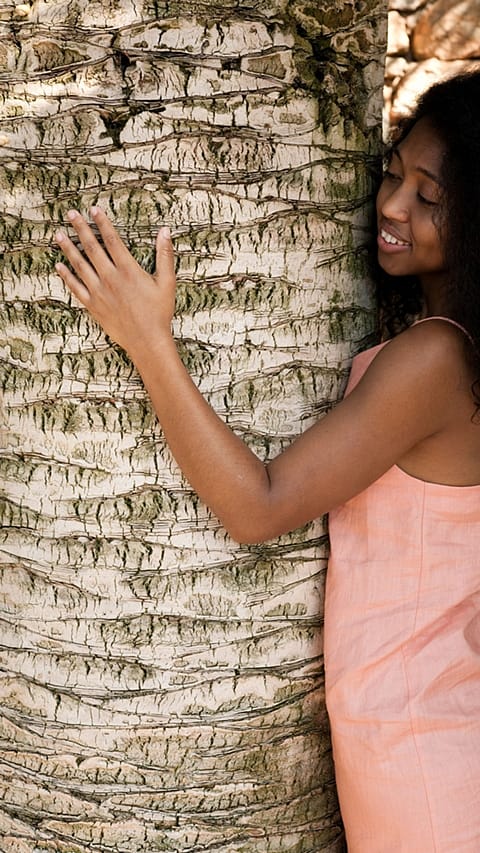 dark skinned woman hugs a tree.