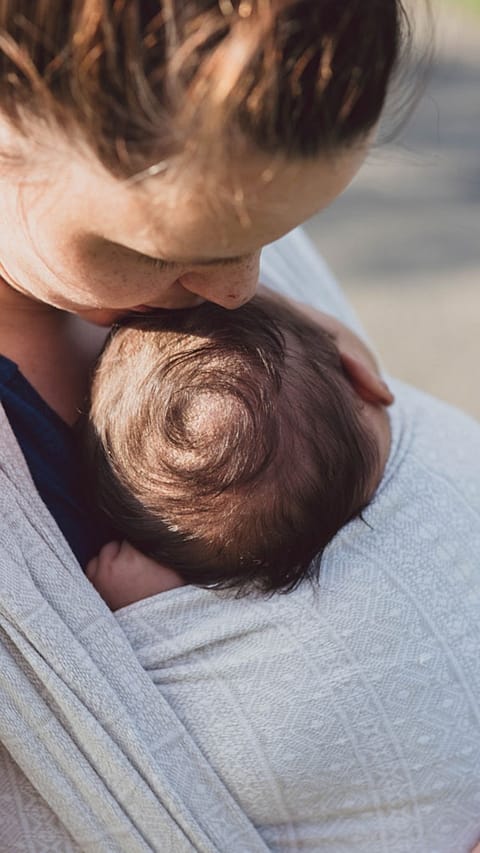 Mother carrying baby in a sling and kissing his head
