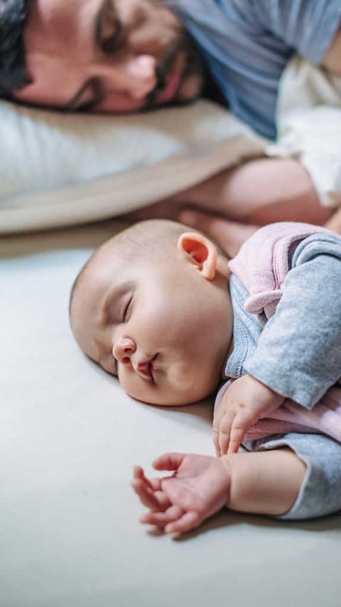 Baby sleep on his sad and dad behind.