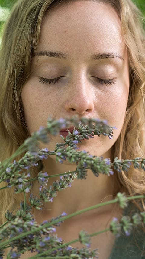 Girl with eye closed smelling flowers.