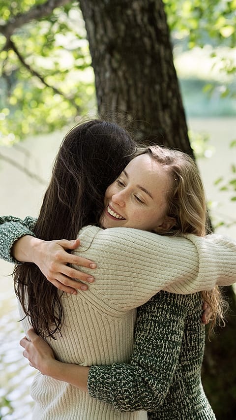 Women hugging next to a tree.