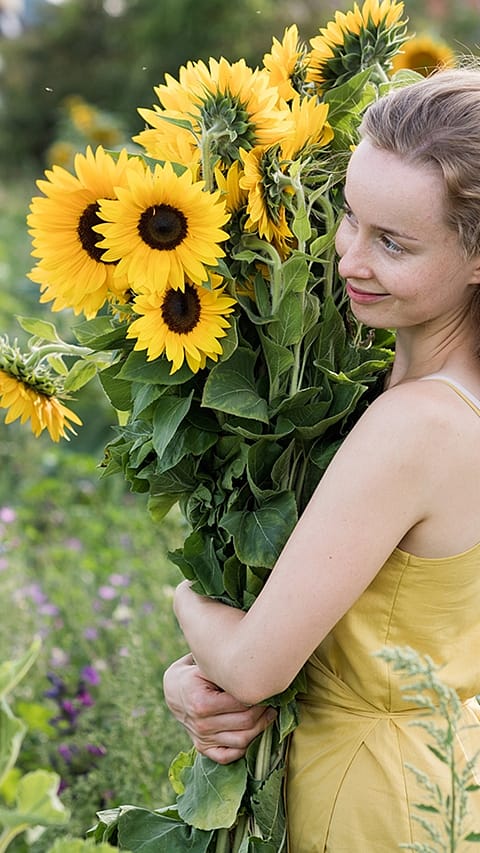 Girl smiling and holding a large bunch sunflowers.