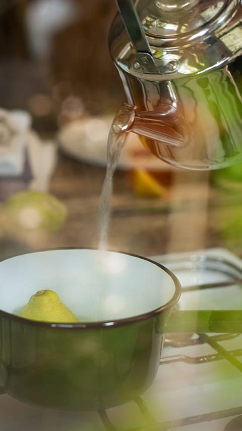 Kettle pouring hot water in a pot with lemon.