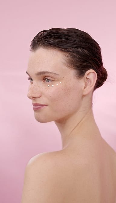 Woman's profile with Smoothing Wild Rose & White Tea cream on her face in a pink background.