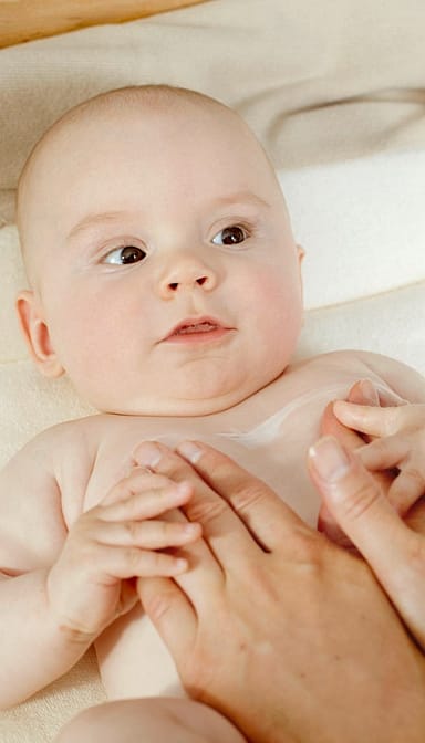 Baby lying down with parents arms on the belly.