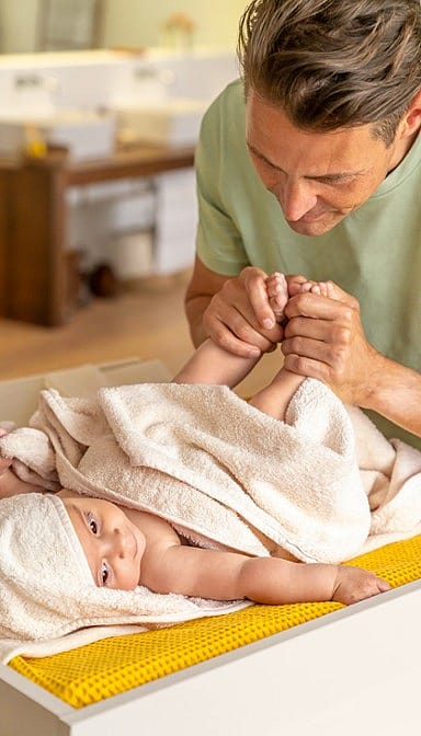 Baby wrapped in a towel and male parent holding his feet.