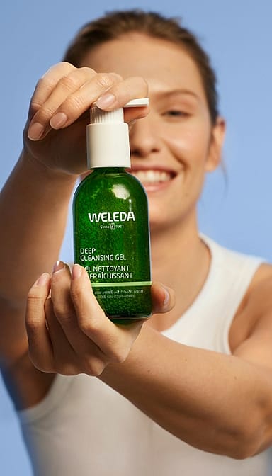 Smiling young woman holding a Deep Cleansing Gel bottle infront of her.