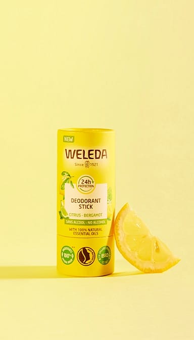 Deodorant Stick Citrus-Bergamot next to a slice of lemon, against yellow background.