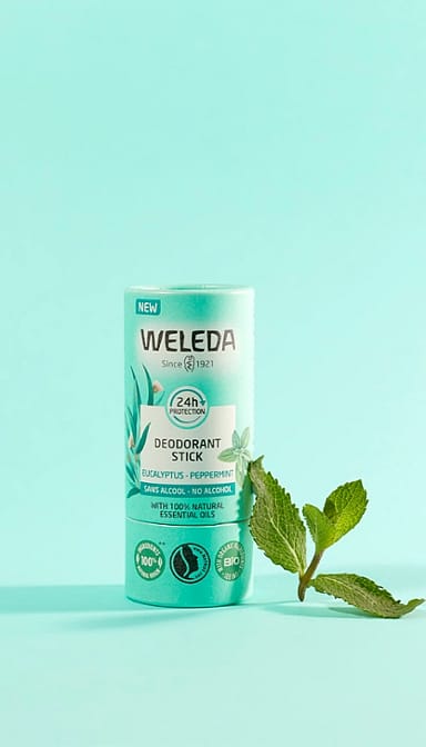 Deodorant Stick Eucalyptus next to peppermint leave, against turquoise background.