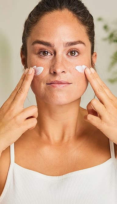 woman applying cream to her face with both hands