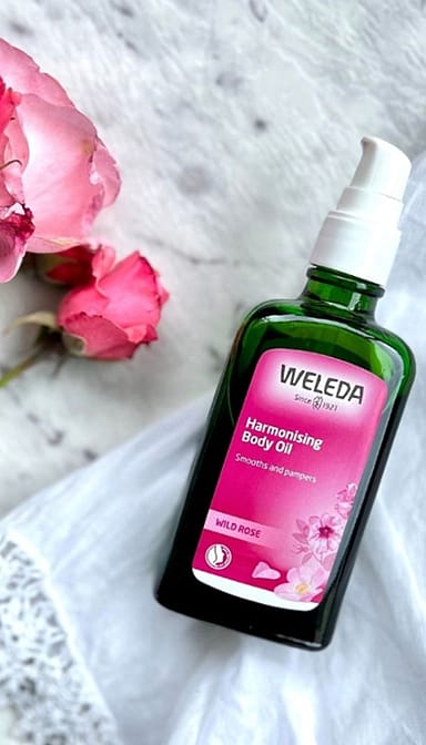 Harmonising Body Oil Wild Rose next to roses.
