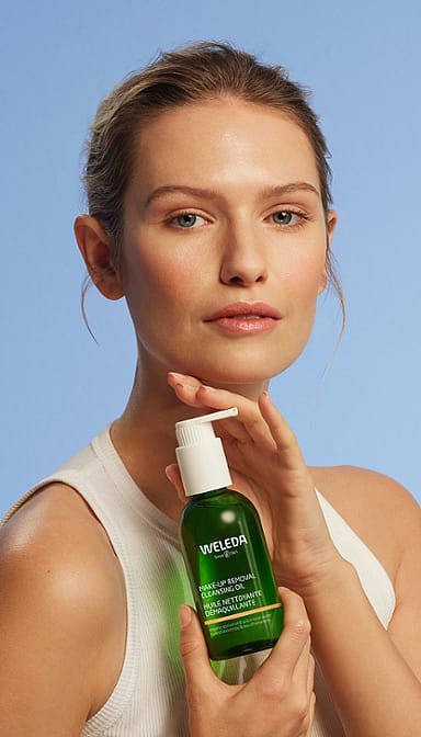 Young woman holdng a bottle of Make-up Removal Cleansing Oil on a light blue background.