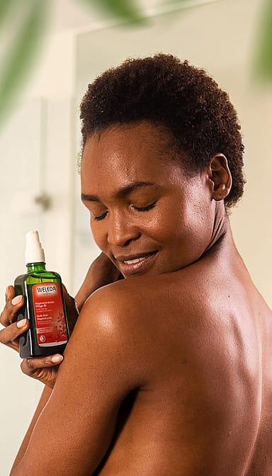 African American woman with her eyes closed holding a bottle of Regenerating Body Oil.