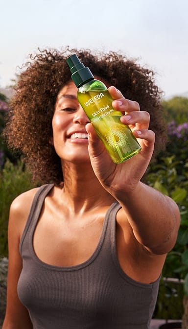 Dark Skin woman holding Skin Food Ultra-Light Dry Oil infront of her.