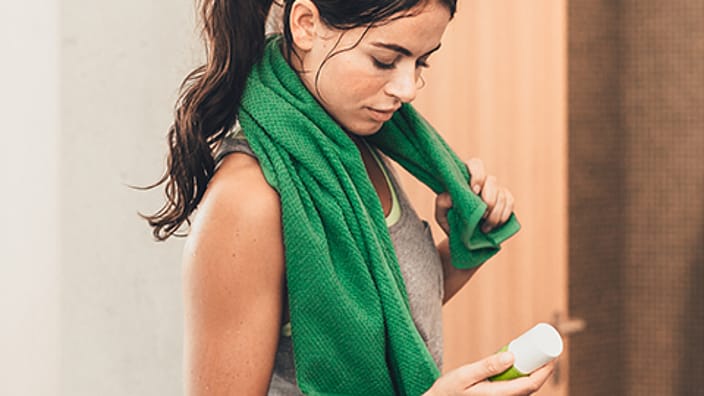 Woman holding a deodorant with a green towel around her
