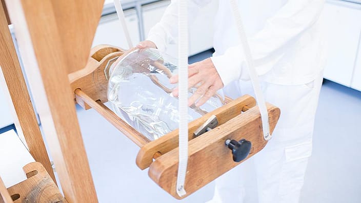 Person holding a potentising glass bottle on a wooden machine.