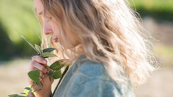 Blonde girl smelling plants side on.