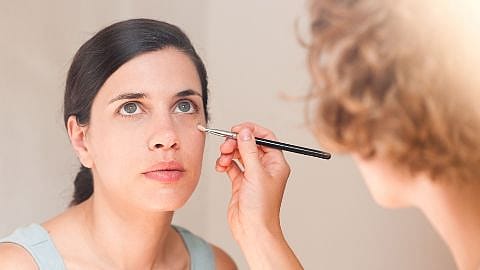 woman having makeup applied under her eye with a brush by another person.