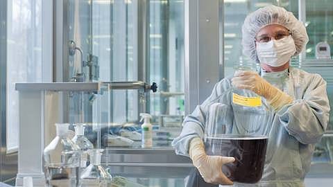 Lab assistant holding a large transparent container filled with a dark liquid