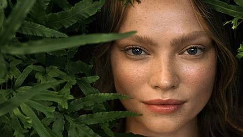 Woman's face next to green leafs.