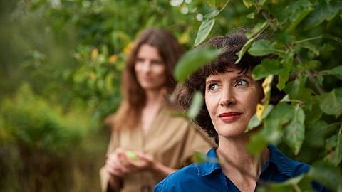 Women standing behind tree leaves.