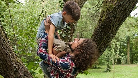 Man holding a child above his arms in a forest.