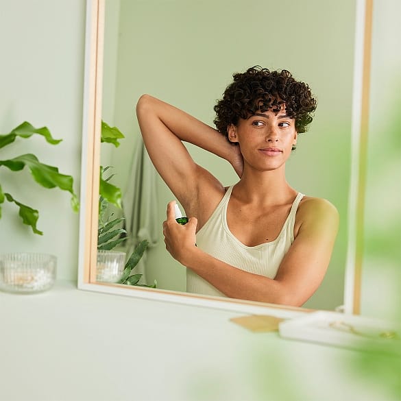 Woman infront of the mirror applying Weleda Spray deodorant.