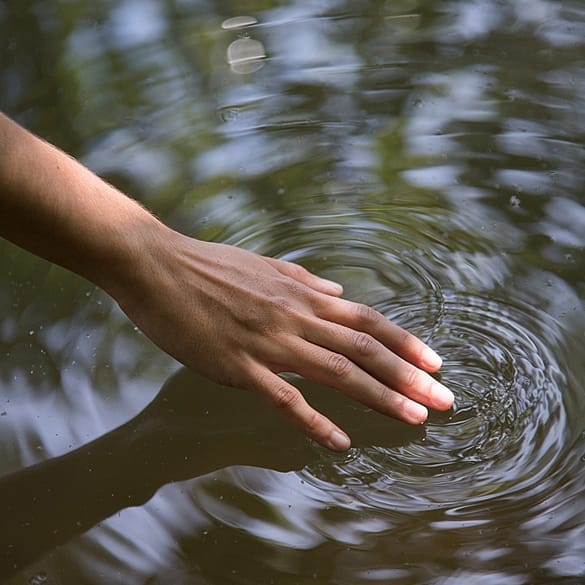 Femenine hand touching water creating a whirlpool.
