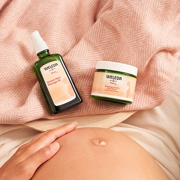 Weleda Stretch Mark Body Butter and Stretch Mark Massage Oil layed on a bed with a pregnant belly