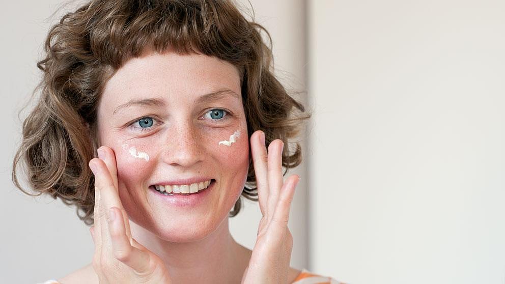 woman is gently applying cream to her face