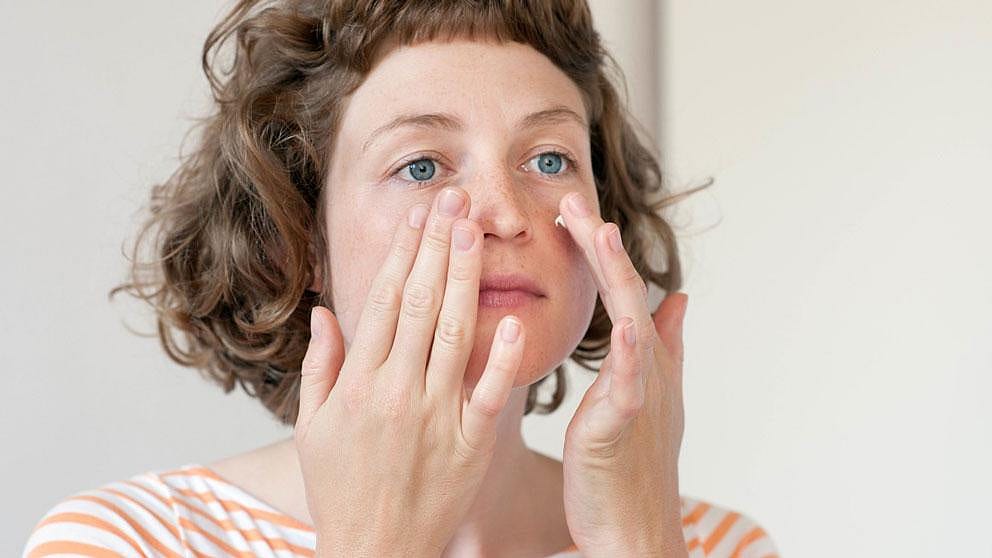 woman is gently applying cream to her face