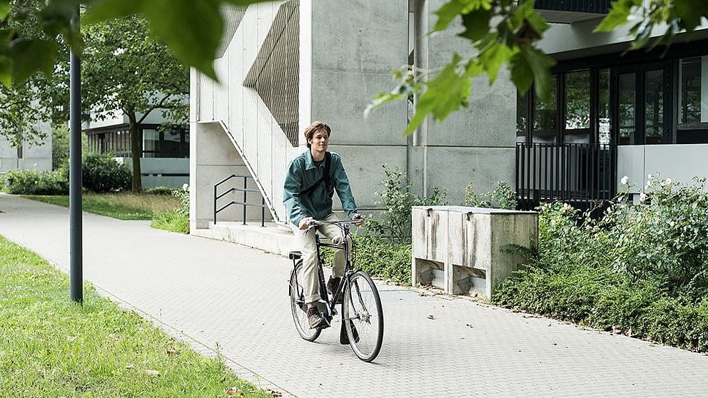 Man riding a bicycle through concrete buildings.