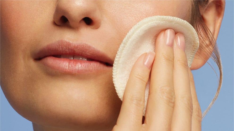 Woman cleansing her face with Weleda One Step Cleanser & Toner and a cotton pad.