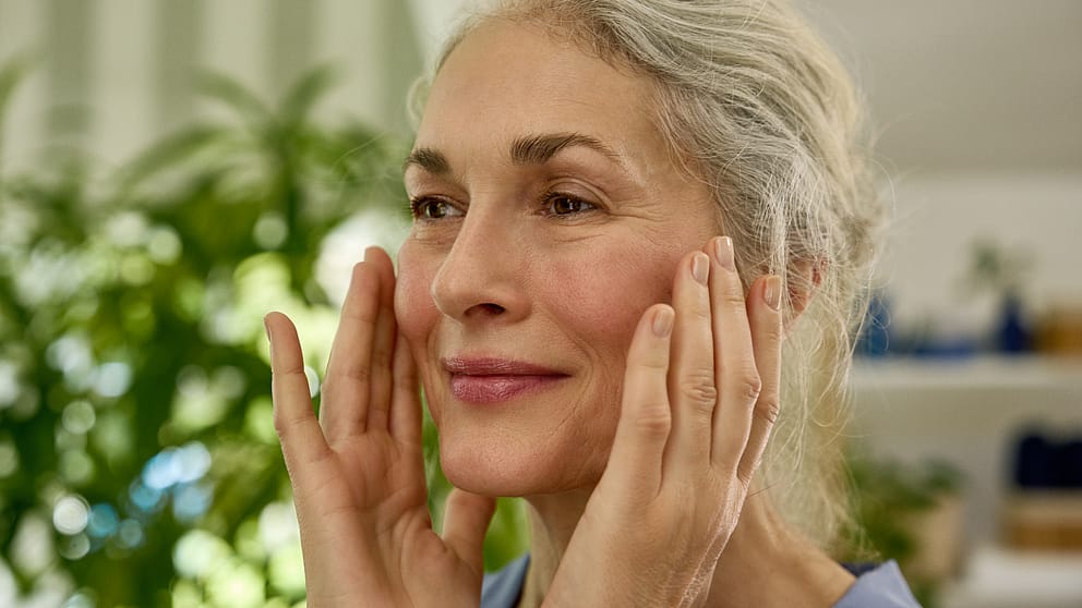 Mature woman applying day cream moisturiser to her face.