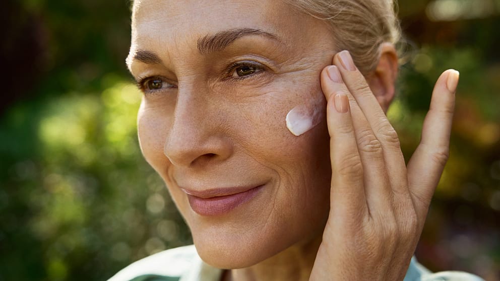 Mature woman applying night cream moisturiser to her face.
