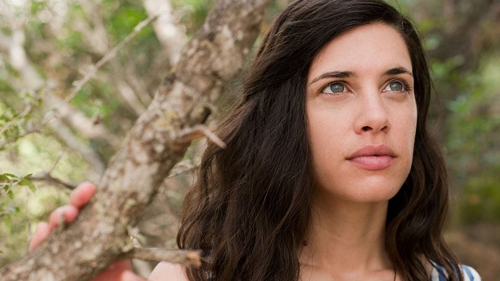 woman in nature, holding onto a tree branch.