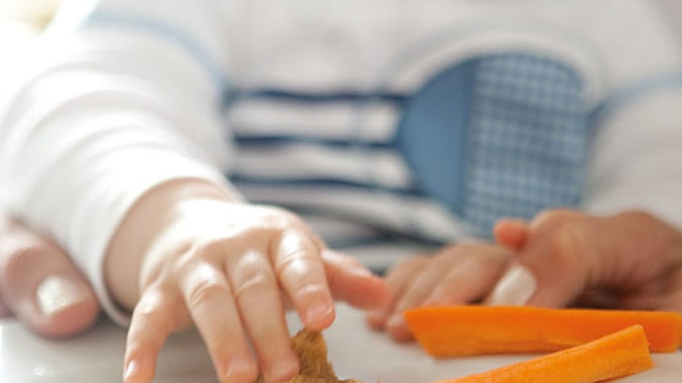 Baby grabbing foods from a plate with his hand.