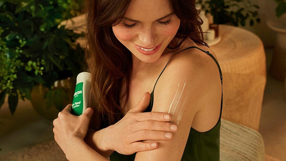 Woman applying Weleda Skin Food Body Lotion onto her arm.