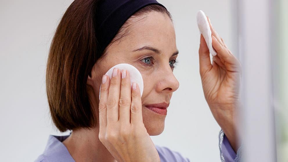 Woman cleansing with Weleda Refining Toner and a cotton pad.