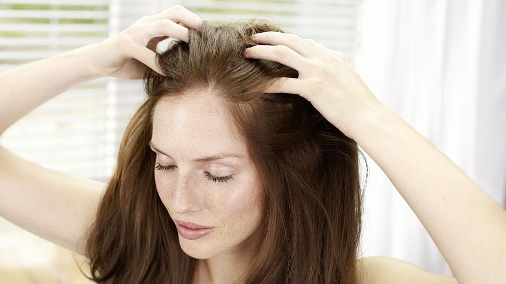 Woman applying Weleda Revitalising Hair Tonic to her hair.