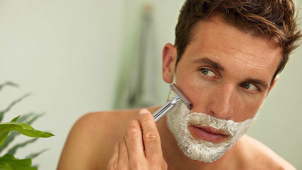 Man with Weleda Shaving Cream on his face holding a razor.